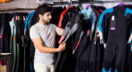 man holding and choosing suit for surfing in the shop