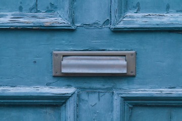 A metal mail slot on an old blue door