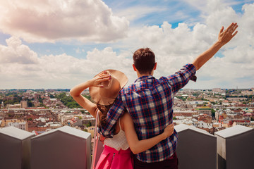 Young couple of tourists with raised hands looking on Lviv, Ukraine from viewpoint
