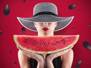 Girl in swimsuit with watermelon in hand and red background with seeds