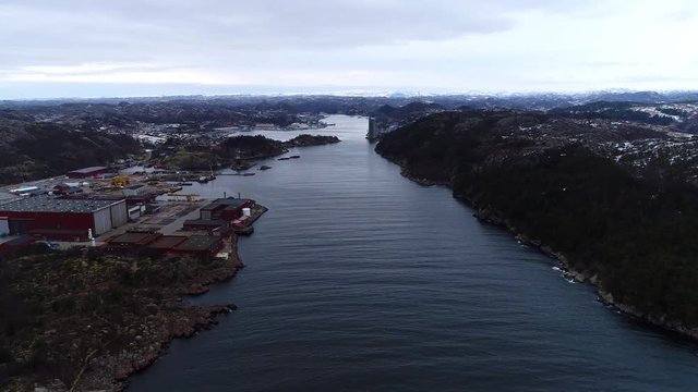Speed up aerial footage of a straight/canal in southern norway during the winter. Flying past shipyards and industry for both Oil & Gas and Fishing.