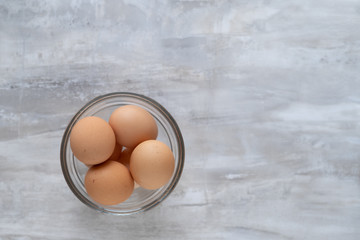 Clear bowl of brown farm eggs on marble background.
