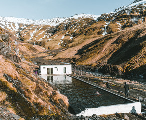 Natural swimming pool Seljavallalaug in iceland with man in water and snowy weather and mountains all around. Sunny weather and blue sky.