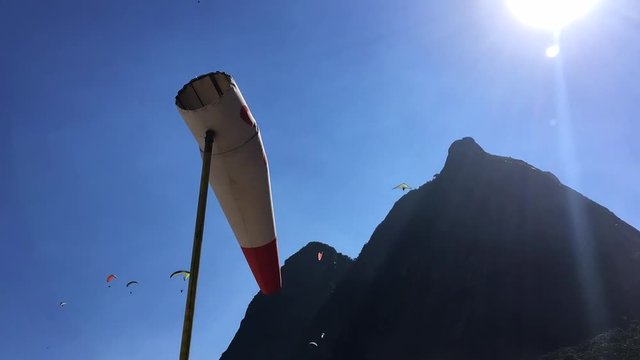 Hang gliders and paragliders flying above a time-lapse windsock in Rio de Janeiro, Brazil