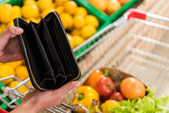 Cropped Image Of Woman Showing Empty Wallet Near Shopping Trolley In Grocery Store