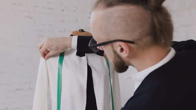Portrait of a tailor while making a white jacket using the tape measure. Close-up of a professional caucasian tailor taking measures with measuring line on mannequin while crafting a new fashion
