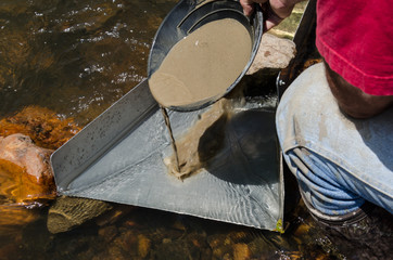 Gold panning with sluice box. Gold prospector feeding mineral rich classified material into sluice...