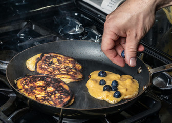 Cooking Paleo Coconut Flour Pancakes in a frying pan with blue berries. © Scott