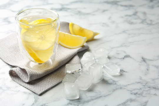 Glass with lemon water and ice cubes on marble table