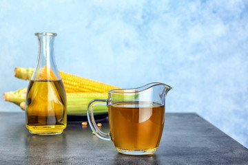 Jug of corn oil on table against color wall