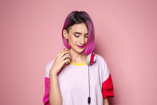Young woman with trendy hairstyle and headphones against color background