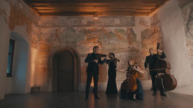 String quartet plays music in a medieval room as the camera pans slightly left
