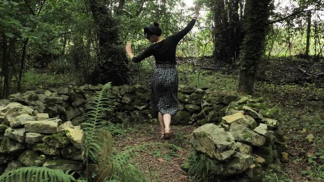 4k beautiful girl in black handmade dress dancing circling in a small big stone scene in a deep green forest celtic style slow motion