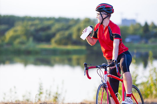 Male Cyclist Having a Rest. Drinking Refreshing Liquid from the Bottle. Shot Made Outdoors. Horizontal Image