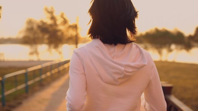 back view woman running at dawn slow motion. brunette wearing white hoodie jogging in the early morning. sunlight in hair. healthy lifestyle