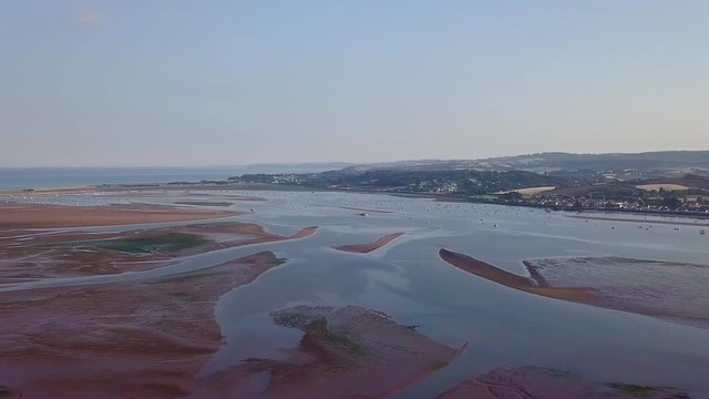 Panning from right to left close to shore from the beach in Lympstone England. The water is filled with water grass and other water plants. In the distance one can see the beach and housing.