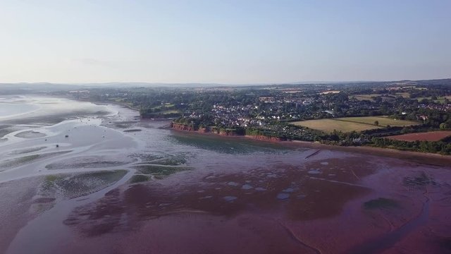 Flying towards the coast of Lympstone England during the day. Patches of agricultural land and the rock formation on the beach is visible.