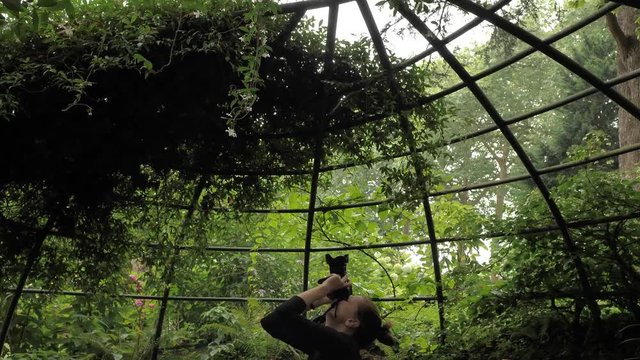 4k beautiful girl in black handmade dress standing inside of oval summer garden metal arbor construction shooting photo with dsl premium objetive in slow motion round moving motion camera