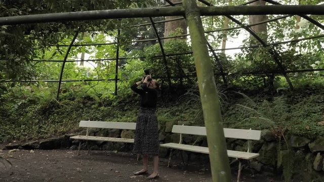 4k beautiful girl in black handmade dress standing inside of oval summer garden metal arbor construction shooting photo with dsl premium objetive in slow motion round moving motion camera