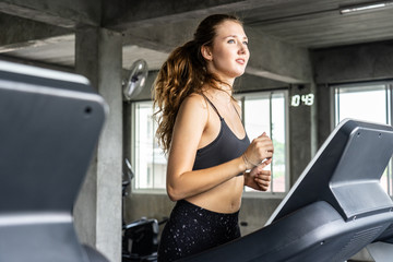 Cute young woman exercising on  treadmill at a gym.Active young woman running on treadmill. smile...