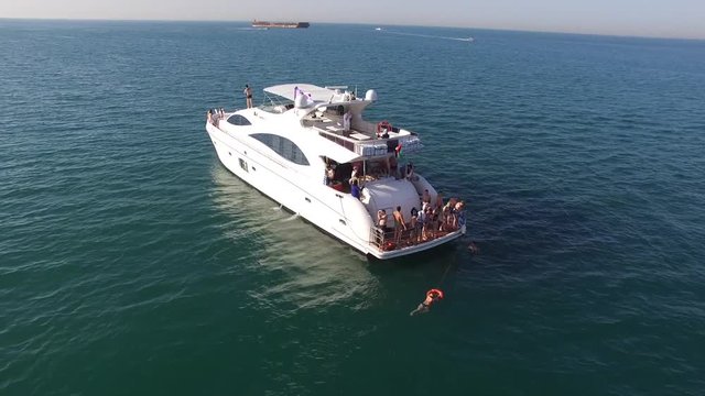 Aerial view of yacht or boat with people cruising at open sea. Stock. Aerial view of a yacht in a crystal clear sea, with people ready to dive in the open sea