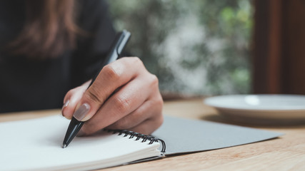 Closeup image of a woman's hand writing down on a white blank notebook on wooden table
