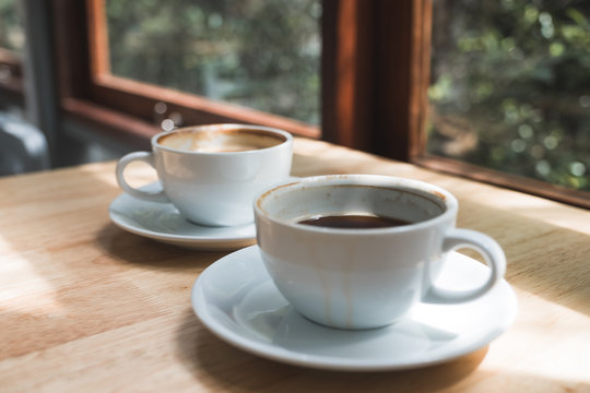 Closeup image of two white cups of hot coffee on wooden table in cafe