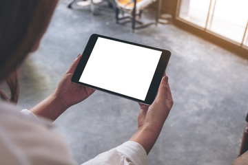 Top view mockup image of a woman sitting and holding black tablet pc with blank white desktop screen in cafe