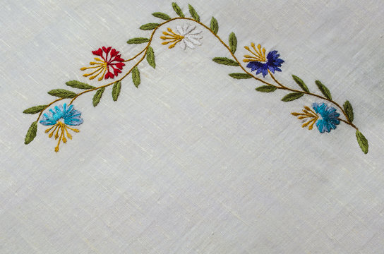 Corner  with border of undulating  branches with the wild flowers cornflowers and leaves on a rough cotton fabric




