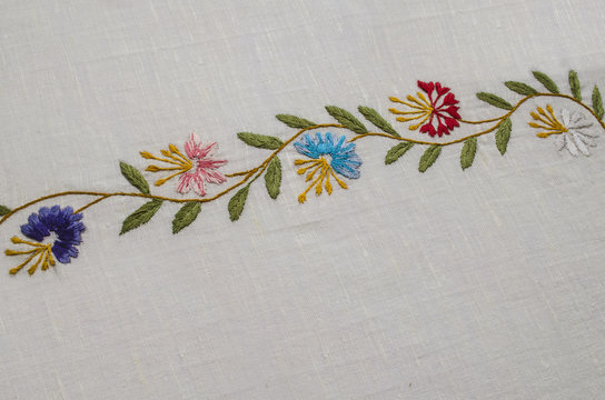 Border of undulating  branches with the field
 flowers cornflowers and leaves on a rough cotton fabric



