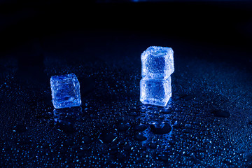 Blue  ice cubes on black wet table.