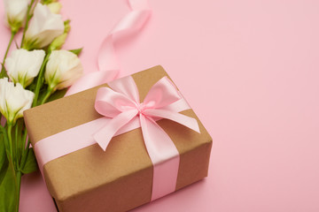 Present box with pink bow and flowers on pink background