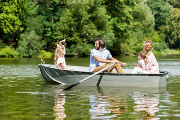 Side view of beautiful young family riding boat on river at park on sunny day
