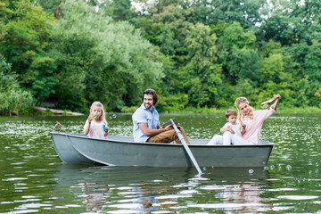 Fototapeta na wymiar smiling young family spending time together in boat on lake at park