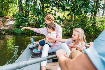 Fototapeta na wymiar Beautiful young family riding boat on lake and pointing somewhere at park