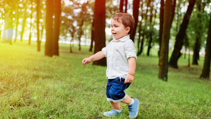 happy little kid in white shirt and denim shorts running by park