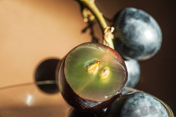 A bunch of dark blue grapes on a dark background in the conditions of artificial hard lighting close up. Grapes, cut in half, grape seeds