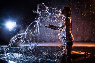 Obraz premium Girl with wet hair in the white shirt, water drops around and dark wall background illuminated by light