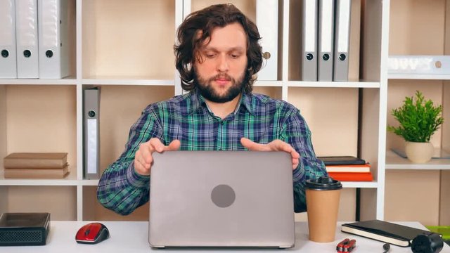 Young professional has finished his work. The man closes his laptop and smiles.