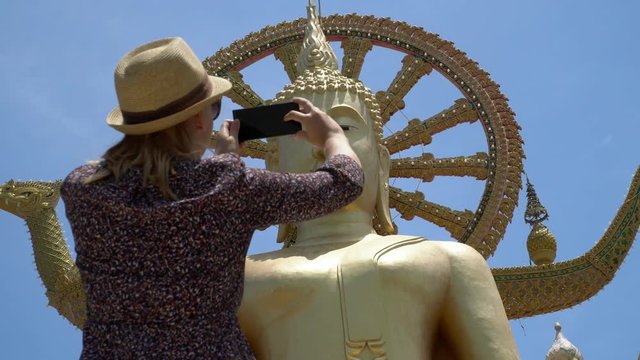 Young Caucasian Female Tourist Taking Mobile Photo of Big Buddha Statue - Symbol and Main Landmark of Samui Island in Thailand. Tourism and Sightseeing