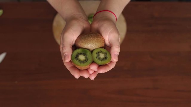 Close-up of a girl holding a juicy ripe cut kiwi on brown wooden background. Slow motion.