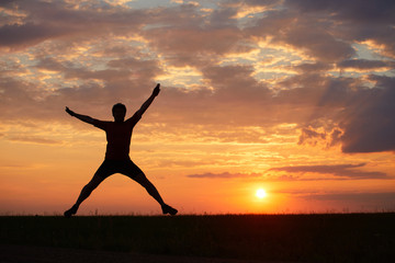 Silhouette of a young man jumping against the sunset with a sense of joy of happiness and freedom