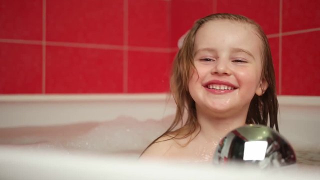 Little girl playing with shower attachment while taking the bath. Happy child girl in the shower. Positive little girl having bath with bubbles in bathtub