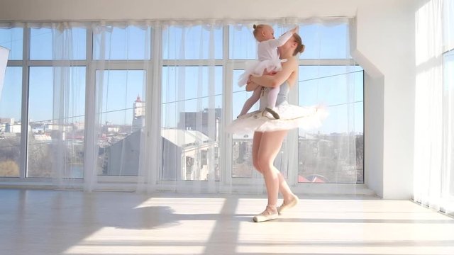 Young graceful ballerina in white tutu dancer and holding on hands her little daughter