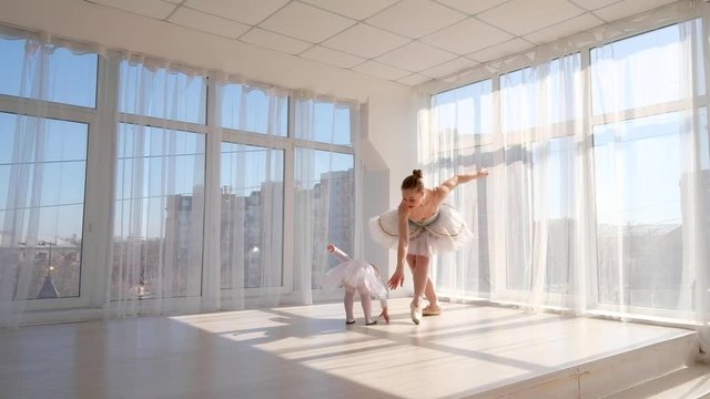 Young gorgeous ballerina teaches her little daughter dancing in studio. Happy ballerina with her child practice a ballet moves. Mother and daughter dancing ballet