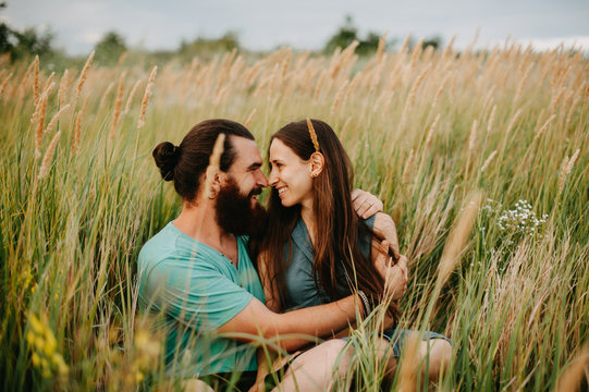 Happy couple looking at each other on a field outdoors smiling. In love bearded man with a long haired girl.