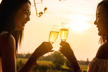 Two beautiful asian women toss white wine of champange in with warm sunset light