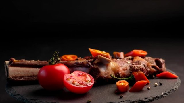 Grilled beef steak on bone with tomatoes rotating on the stone cutting board