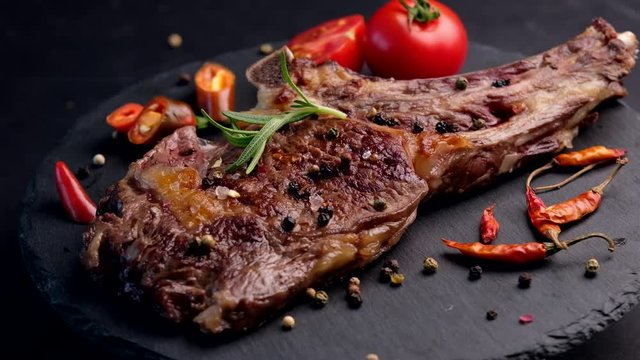Close-up of grilled beef steak on bone with tomatoes rotating on the stone cutting board