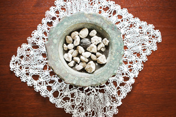Heap of stones and dark sand in ceramic bowl with decorative home-made tablecloth beneath.